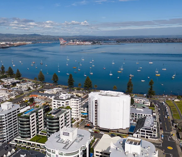 An aerial view shows a coastal city and marina filled with sailboats.