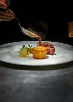 A chef finishes a gourmet fish dish with sauce and fresh garnishes.