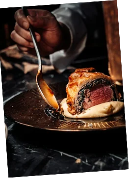 A chef spoons sauce around a carefully plated beef Wellington.