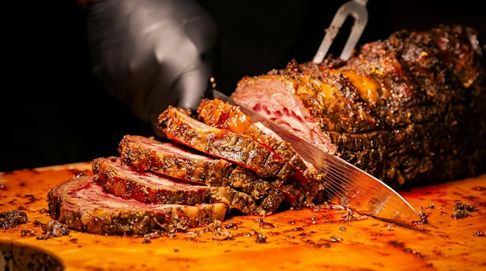 A gloved chef slices a seasoned roast into thick portions.