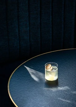 A small cocktail sits on a round blue table under dramatic lighting.