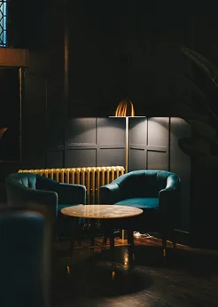 A moody lounge contains teal chairs, small tables, and warm ambient lighting.