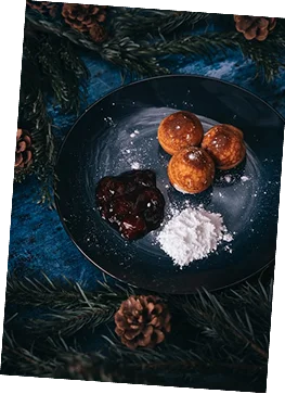 Fried dough balls are arranged on a dark plate with several dips.