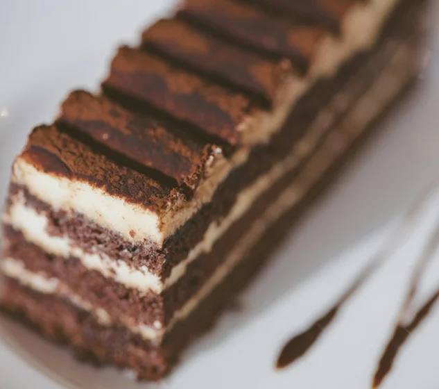 A close-up of a layered chocolate dessert with light cream filling, topped with cocoa powder and served on a white plate.