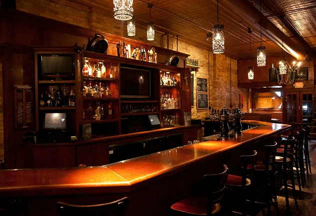 An empty traditional wooden bar is illuminated by warm pendant lights.